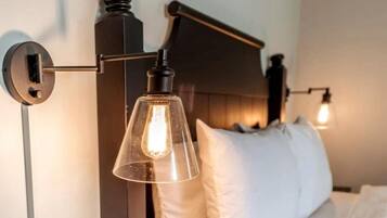 Una cama con almohadas blancas y una lámpara colgante de cristal transparente.