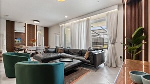A modern living room with a sectional sofa, teal armchairs, and a dining area with a table and chairs.