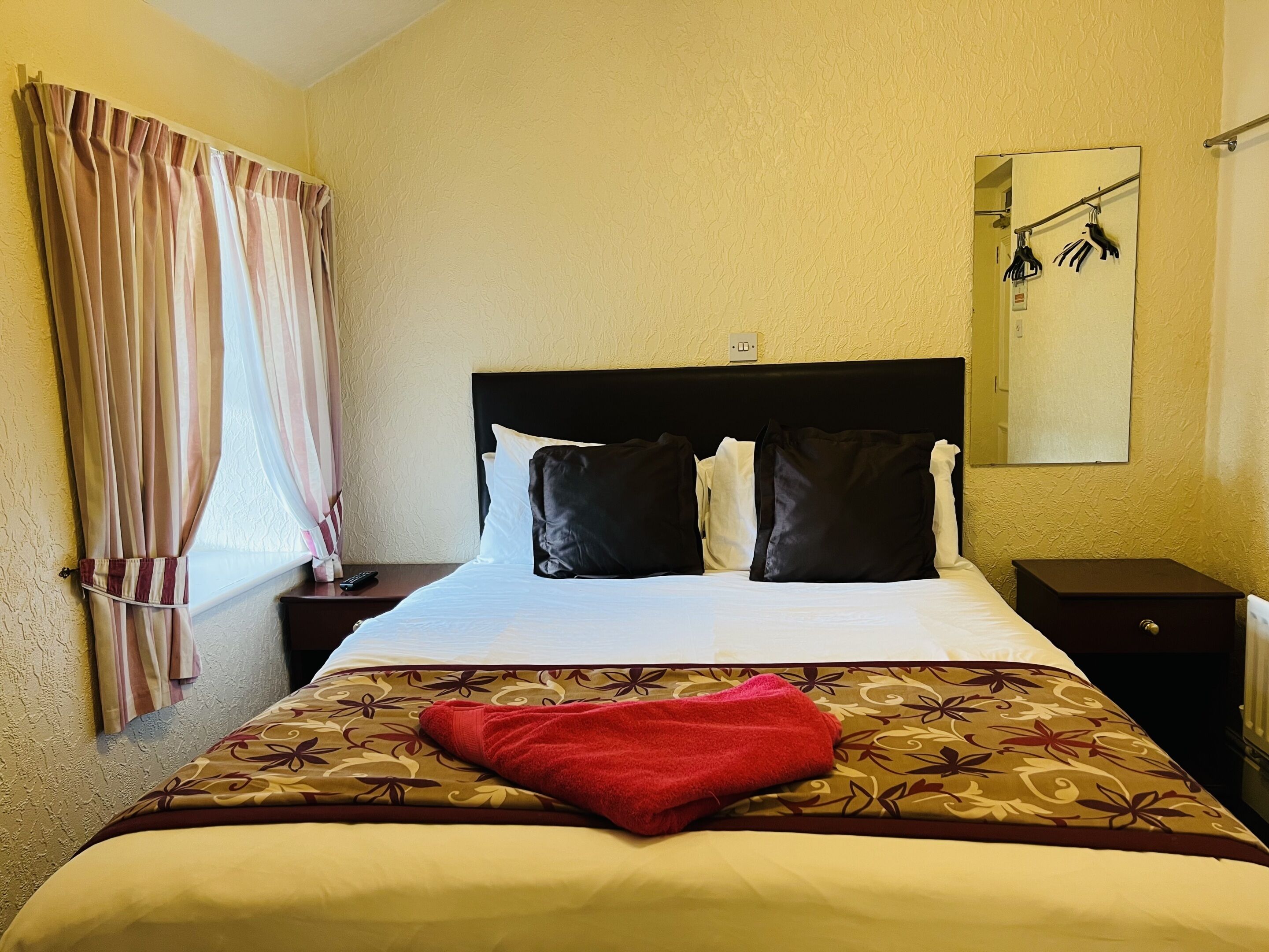Habitación de hotel con cama, mesita de noche, espejo y ventana con cortinas.