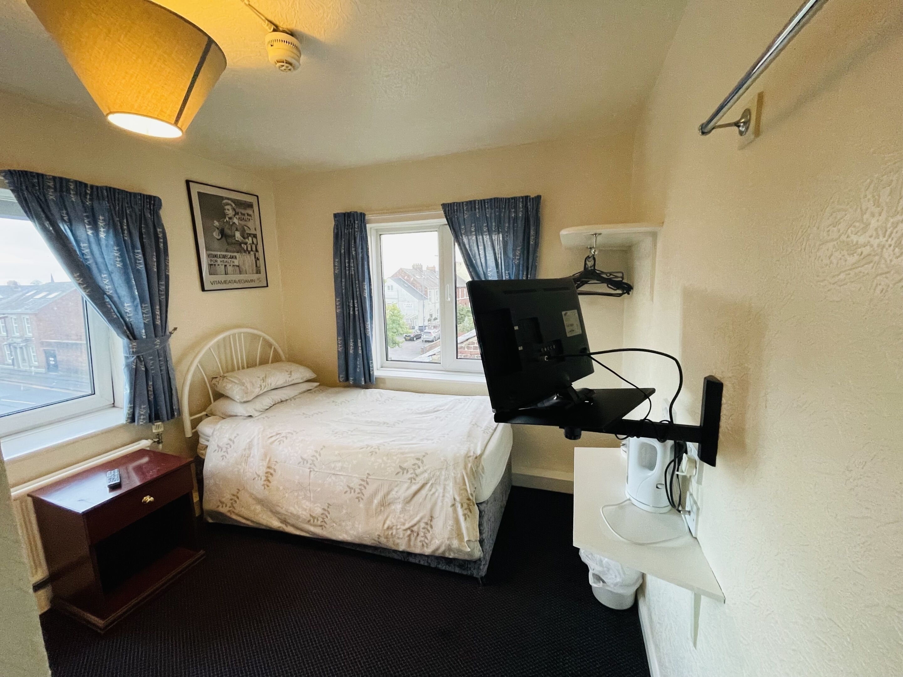 Une chambre d’hôtel comprenant un lit, un bureau, une chaise, un téléviseur fixé au mur et une fenêtre avec des rideaux.