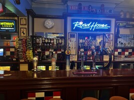 A bar with a neon sign reading "Road House," various beer taps, and a clock on the wall.
