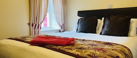 A hotel room with a bed, striped curtains, a headboard, and a window.
