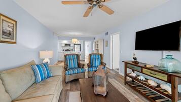 A living room with a sofa, two armchairs, a coffee table, a TV, and a ceiling fan.