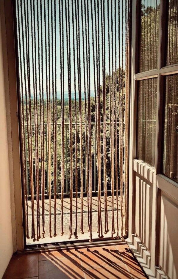 Een balkon met een versierd vloertje, uitzicht op bomen en een raam met een metalen hekwerk.