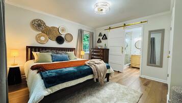 A bedroom with a bed, bedside tables, a dresser, a mirror, and a door leading to a bathroom.