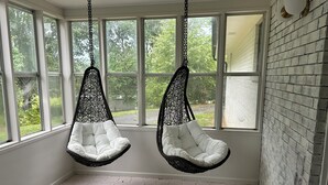A room with two hanging chairs, large windows, a brick wall, and a hexagonal tile floor. - Escape to Bell Branch Place: Where Relaxation Meets Comfort (Cleveland)