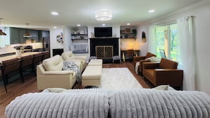 A modern living room with a sofa, armchairs, a coffee table, and a fireplace. There is a kitchen area with cabinets and a dining table. - Escape to Bell Branch Place: Where Relaxation Meets Comfort (Cleveland)