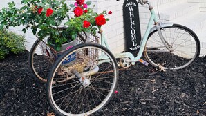 A bicycle with a basket of red flowers parked in front of a white brick building with a 'WELCOME' sign. - Escape to Bell Branch Place: Where Relaxation Meets Comfort (Cleveland)