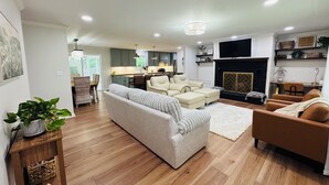 A modern living room with a sofa, armchairs, a fireplace, and a kitchen in the background. - Escape to Bell Branch Place: Where Relaxation Meets Comfort (Cleveland)