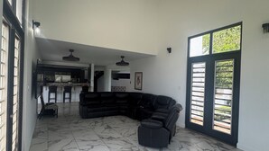 A spacious living area with a curved black sofa, a dining table, and a kitchen in the background. - Coastal Luxury Getaway for Yoga, Golf & Family Fun (Humacao)