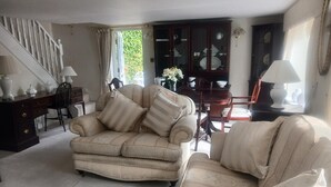 A living room with a beige sofa, a wooden coffee table, and a dining area with a dark wooden cabinet and a chandelier. - Romantic Cottage for two in North Yorkshire (Middlesbrough)