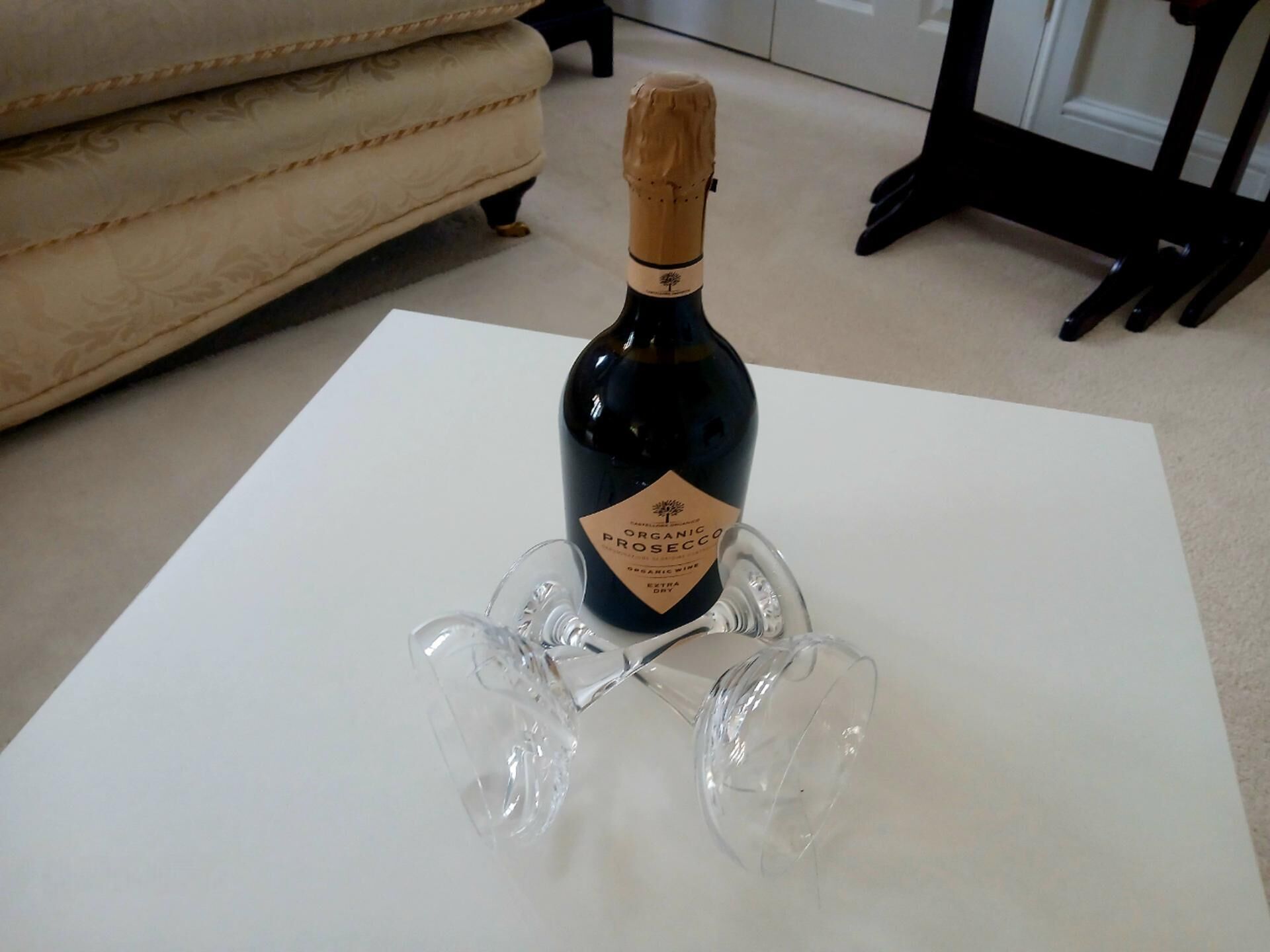 A bottle of organic prosecco on a white table with four wine glasses.