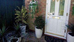 A brick wall with a white door, potted plants, and a hanging flower arrangement. - Romantic Cottage for two in North Yorkshire (Middlesbrough)