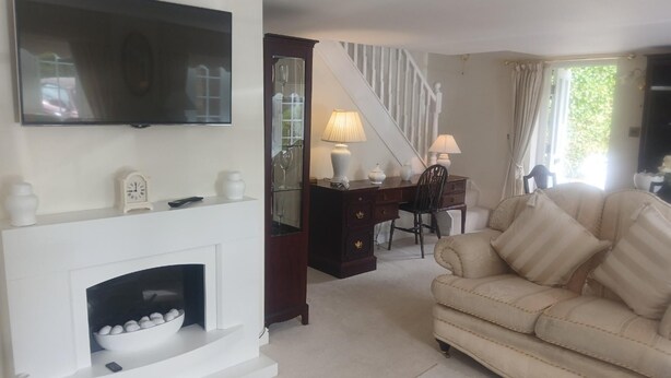 A living room with a fireplace, a sofa, a television, a desk with a lamp, and a staircase. - Romantic Cottage for two in North Yorkshire (Middlesbrough)