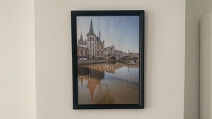 Een ingelijste foto van een historisch gebouw met een brug die in het water wordt weerspiegeld, geplaatst op een marmeren schoorsteenmantel.