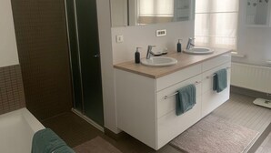 Een moderne badkamer met een douche, twee wasbakken, een grote spiegel en een raam voor natuurlijk licht.
