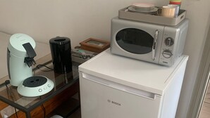 Een kleine keuken met een Bosch koelkast, een koffiezetapparaat, een magnetron en een afvalbak.