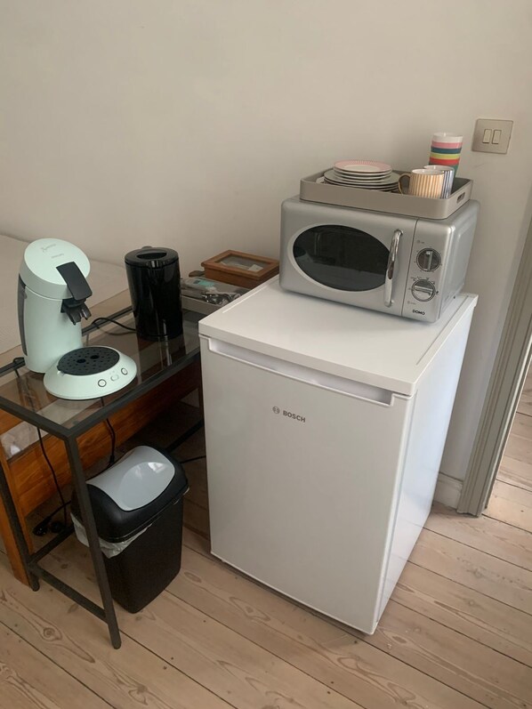 Une petite cuisine équipée comprenant un réfrigérateur Bosch, une machine à café, un four à micro-ondes et une poubelle.