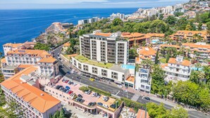 A coastal cityscape with a prominent hotel featuring a rooftop terrace, a parking lot, and a view of the sea. - Infinity View by Madeira Sun Travel (Funchal)