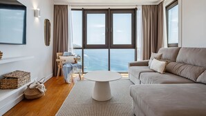 A modern living room with a large window, a round coffee table, a sofa, and a TV mounted on the wall. - Infinity View by Madeira Sun Travel (Funchal)