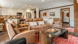 A spacious living room with leather sofas, a glass coffee table, and a kitchen area with modern appliances.