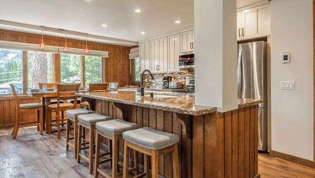 A modern kitchen with wooden cabinets, a stainless steel refrigerator, and a bar area with stools.