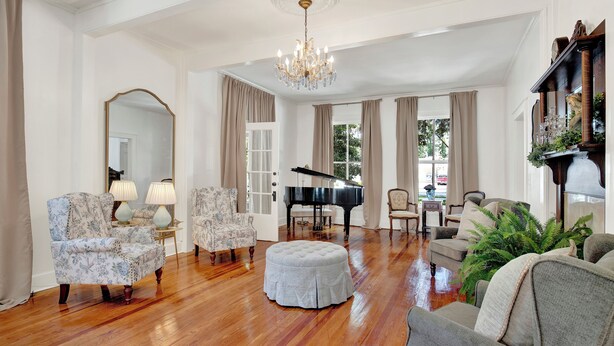 Een ruime woonkamer met een vleugelpiano, elegante stoelen en een kroonluchter.