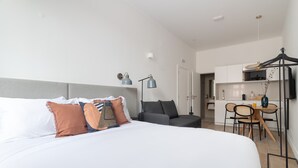 A hotel room with a large bed, a desk with chairs, a kitchenette, and a TV.