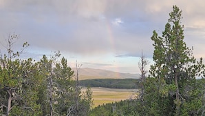 Paisagem arborizada com vista para montanhas distantes e um arco-íris.