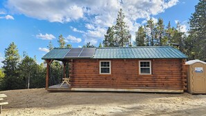 Uma cabana de madeira com telhado de metal, painéis solares e um pequeno banheiro anexo.
