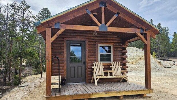 Uma cabana de toras com porta da frente, duas janelas e um alpendre com duas cadeiras Adirondack.