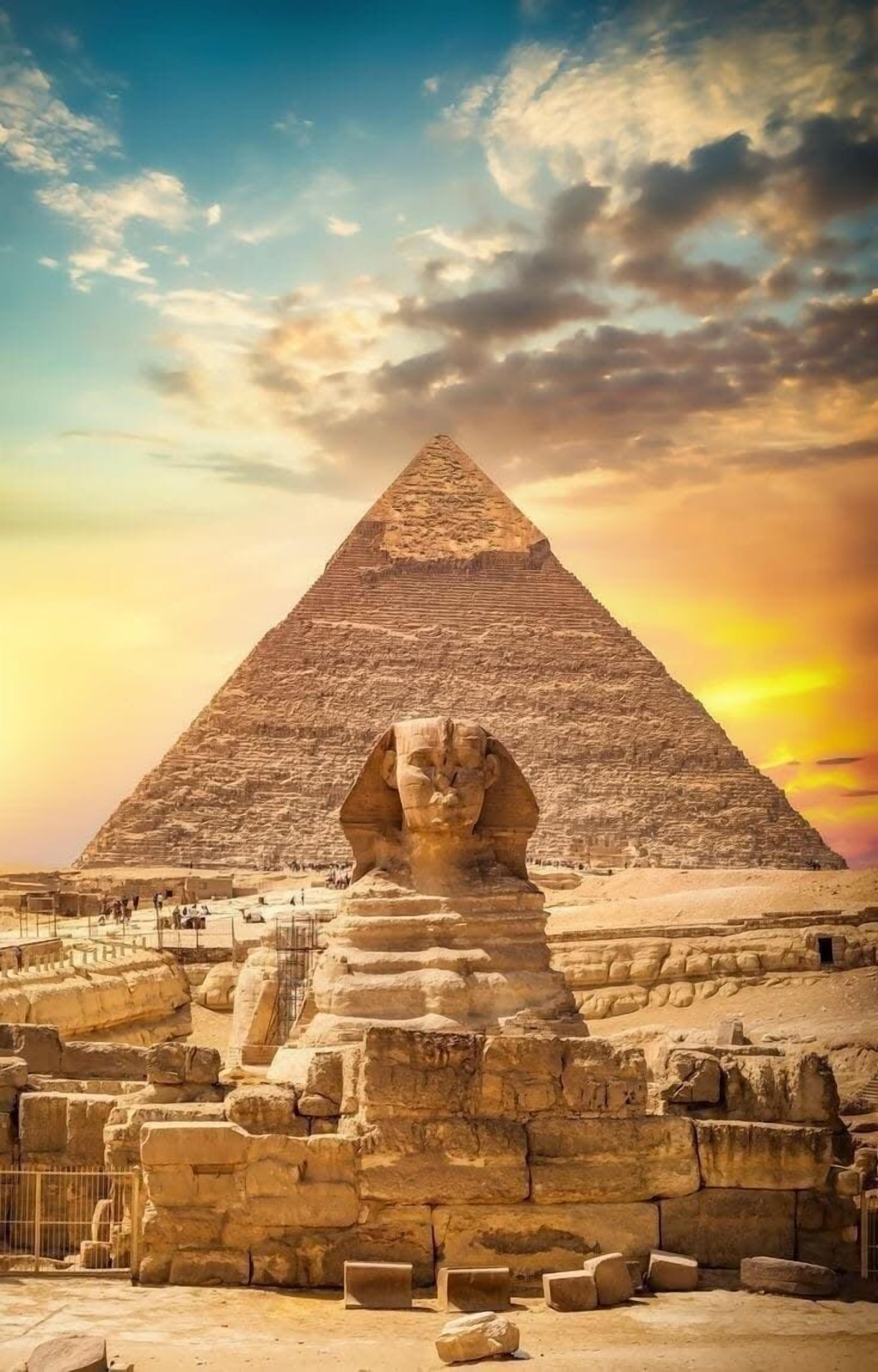 A large pyramid with a sphinx in front, surrounded by ancient ruins.