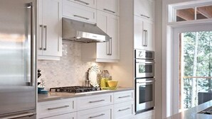 Cozinha moderna com armários brancos, eletrodomésticos de aço inoxidável e vista para o exterior.