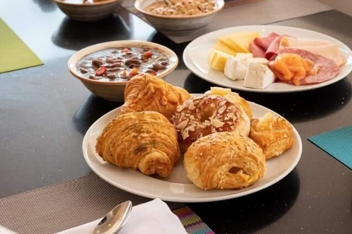 Ein Frühstückstisch mit Croissants, einer Platte Schinken und Käse sowie Schüsseln mit Suppe und Müsli.
