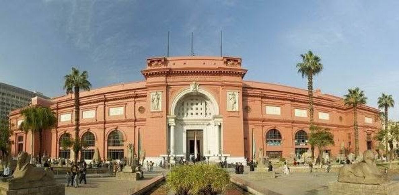 A large, circular building with a central entrance, surrounded by palm trees and a paved plaza.