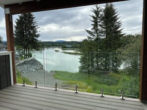 A balcony with a view of a river, surrounded by trees and a grassy area. - Water and mountain view’s in charming Juneau (Juneau)