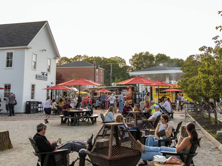 An outdoor seating area with tables and chairs, a white building labeled "Public House" in the background, and a white truck parked on the right.