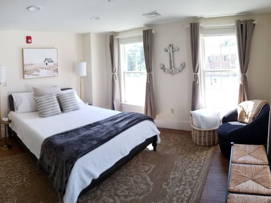 A hotel room with a large bed, a chair, a small table, a potted plant, and a window with curtains.