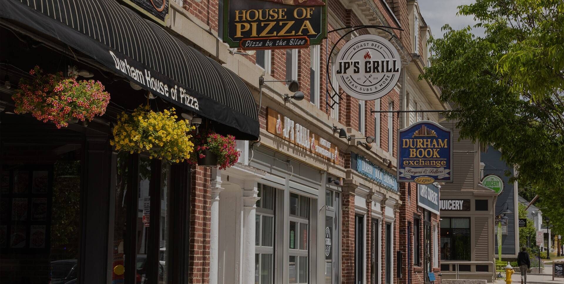 A street view with various shops including House of Pizza, Jp's Grill, Durham Book Exchange, and Juicery.