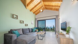 Ein modernes Wohnzimmer mit Ecksofa, Holzboden, Fernseher und einem Balkon mit Blick.