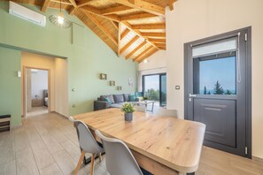 A spacious room with a wooden dining table, grey chairs, a grey sofa, and a large window with a view.