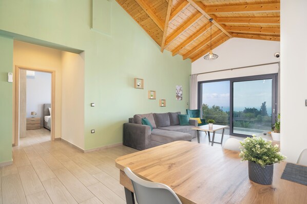 Un salon moderne avec un plafond en bois, un canapé, une table à manger et une grande fenêtre offrant une belle vue.