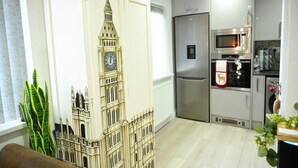 A modern kitchen with a stainless steel refrigerator, microwave, and oven. There is a clock on the wall and a decorative clock with a fox design.