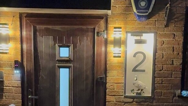 A wooden door with a vertical window, a small ramp leading up to it, and a brick wall with a number '2' sign. - Watermead Retreat Bungalow (Leicester)