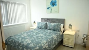 A bedroom with a bed, nightstand, lamp, and a wall painting.
