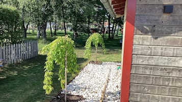 A wooden cabin with a red roof, surrounded by a gravel path and trees.