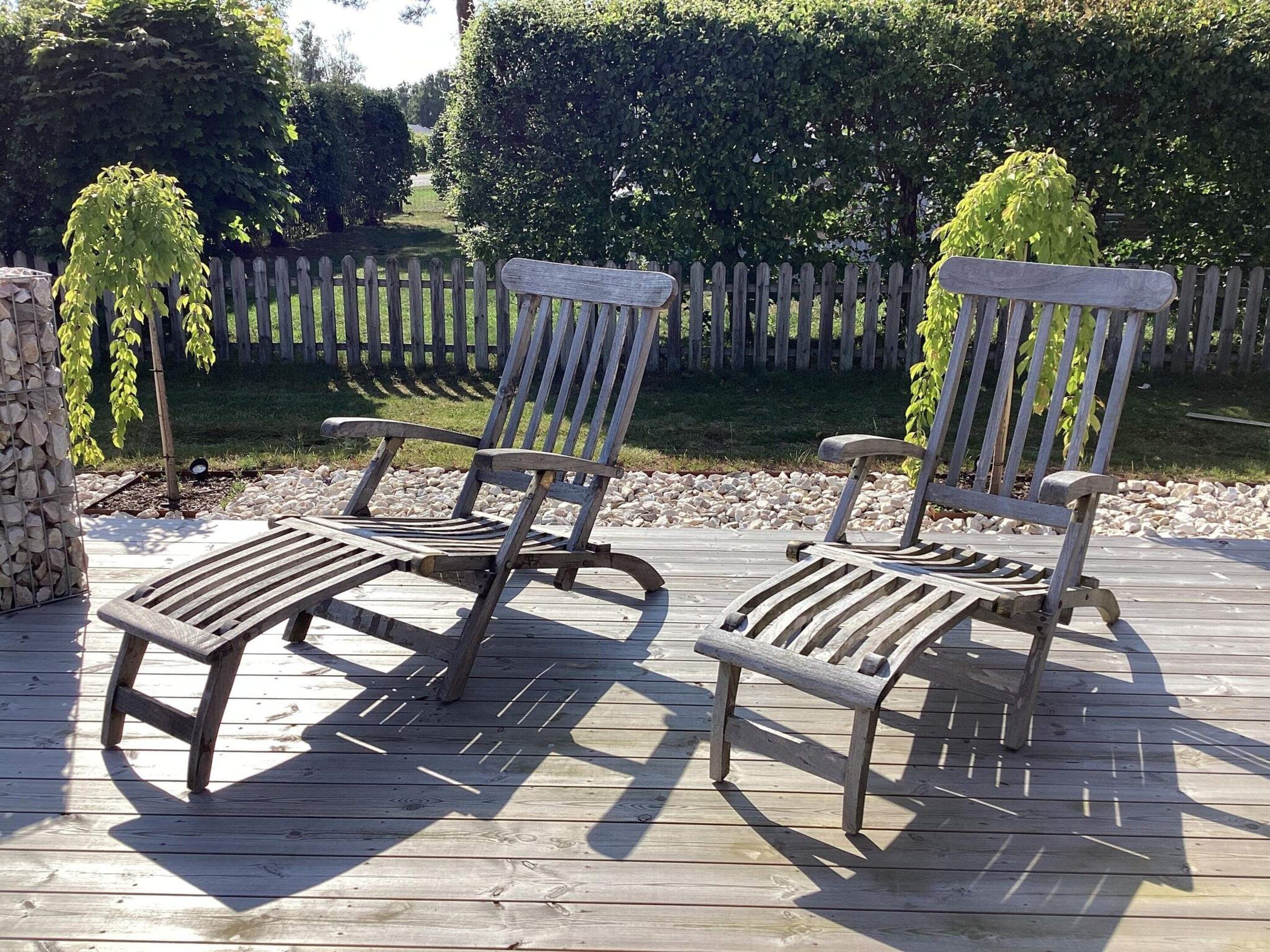 Two wooden lounge chairs on a wooden deck with a stone wall and a wooden fence in the background.
