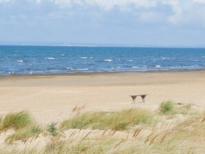 Ein Strand mit sandigem Ufer und einer Wasserfläche. Zwei Steinstrukturen liegen am Strand.