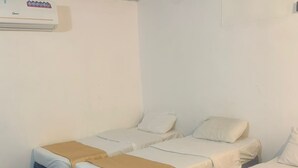 A hotel room with three single beds, each with a blue skirted base and a beige blanket. - Al Awali Economic Apartments (Madinah)