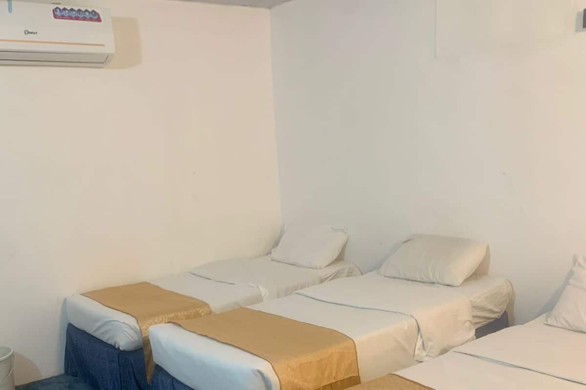 A hotel room with three single beds, each with a blue skirted base and a beige blanket.